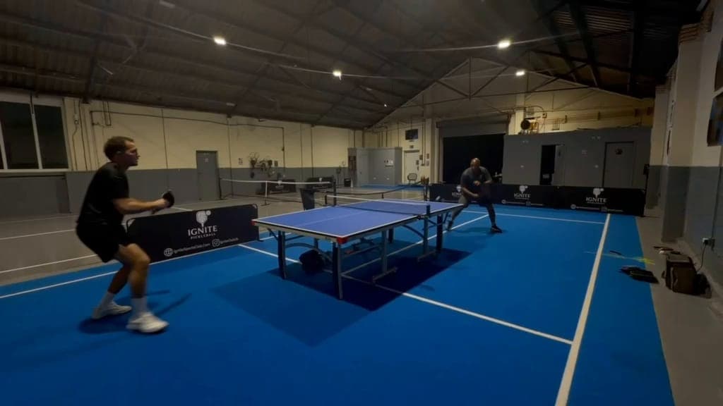 A table tennis rally in full swing on the blue floor of the hall at Ignite at night