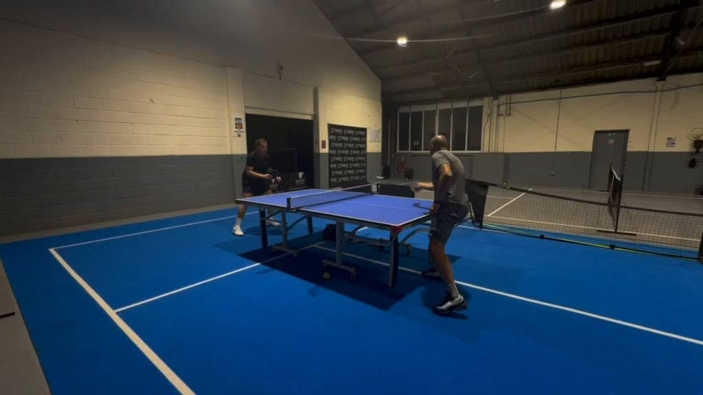 Table tennis on the blue floor of the hall at Ignite, with the court banners and nets behind