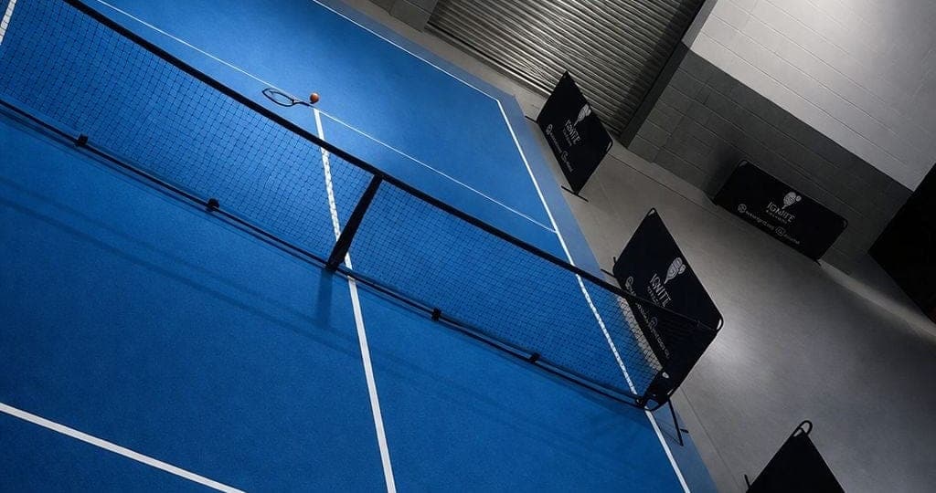 The blue touch tennis court at Ignite from above the baseline, with the net and court banners