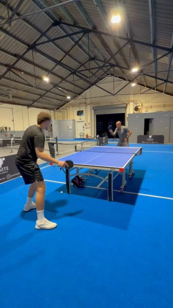 A player returns a shot at a blue table tennis table on the blue floor at Ignite at night