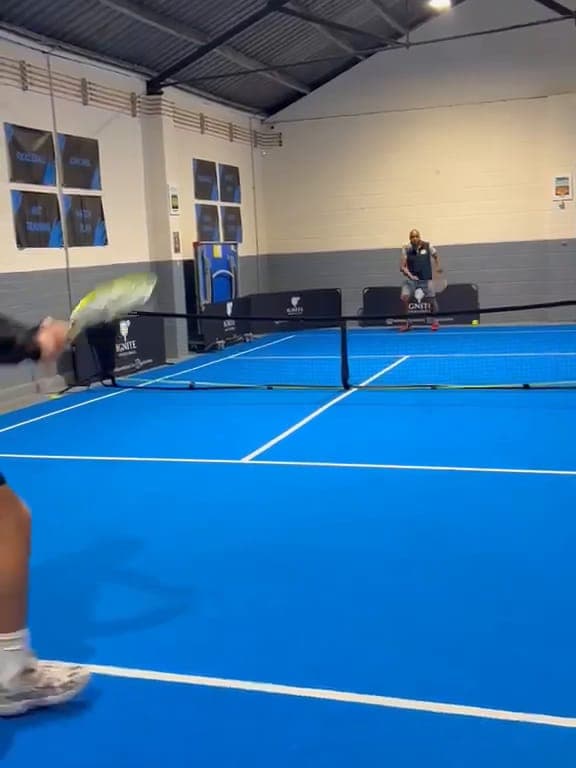 A player follows through on a forehand on the blue court, with an opponent waiting across the net